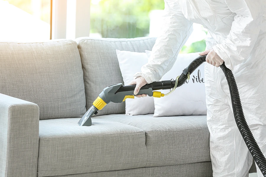 biohazard technician sanitizing a grey couch